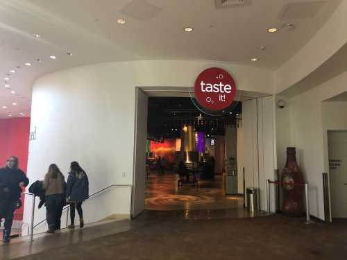 Entrance to a venue labeled "taste it!" with people walking inside and colorful lights visible in the background.