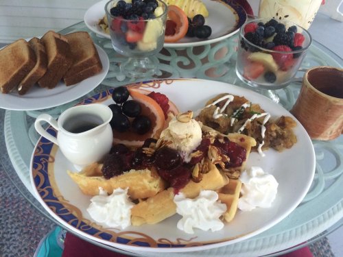 A plate of waffles topped with fruit, ice cream, and whipped cream, accompanied by a side of toast and fruit cups.