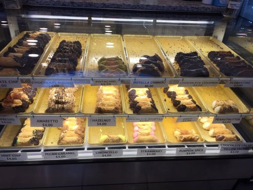 Display case filled with various cannoli and desserts, including flavors like hazelnut, pistachio, and chocolate.