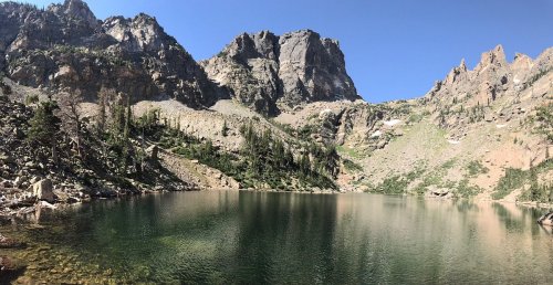 A serene mountain lake surrounded by rugged peaks and lush greenery under a clear blue sky.
