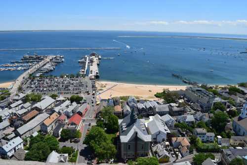 Aerial view of a coastal town with a marina, beach, and blue waters under a clear sky.