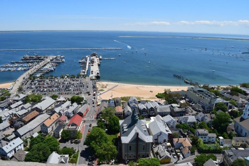 Aerial view of a coastal town with a marina, beach, and blue waters under a clear sky.