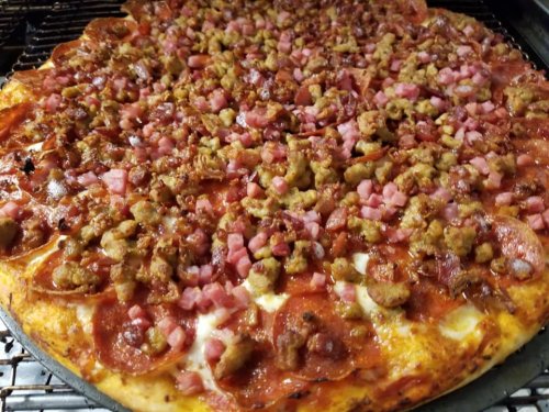 A close-up of a pizza topped with pepperoni, sausage, and diced ham on a golden crust.