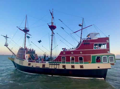 A colorful pirate ship sails on calm waters under a clear blue sky, with people enjoying the view on deck.