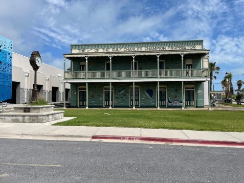Historic two-story building with green walls and decorative murals, featuring a clock tower nearby under a blue sky.