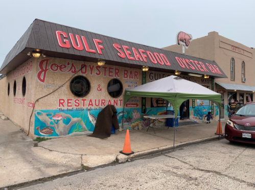 Exterior of Joe's Oyster Bar and Restaurant, featuring colorful murals and a tent outside, with a car parked nearby.