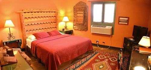 Cozy bedroom with a wooden headboard, warm orange walls, a patterned rug, and soft lighting from bedside lamps.