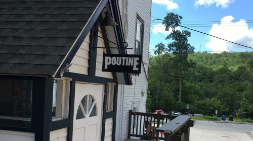 A building with a sign reading "Poutine" against a backdrop of trees and a blue sky.