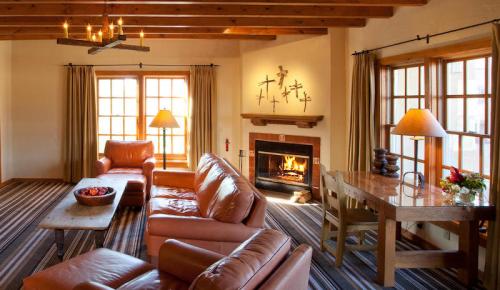 Cozy living room with leather furniture, a fireplace, and large windows, featuring warm lighting and a wooden dining table.