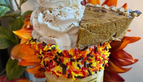 A creamy dessert topped with whipped cream, a slice of pie, and colorful sprinkles, surrounded by autumn flowers.