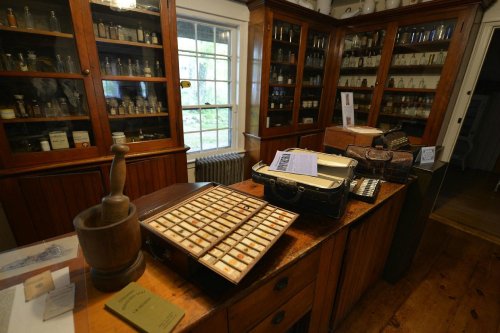 A vintage apothecary with wooden cabinets, glass jars, and a wooden mortar and pestle on a table.