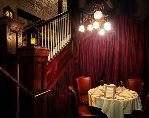 Cozy restaurant corner with a table set for two, warm lighting, and a staircase in the background.