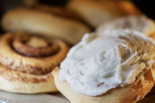 Close-up of freshly baked cinnamon rolls with creamy white frosting, set against a background of more rolls.