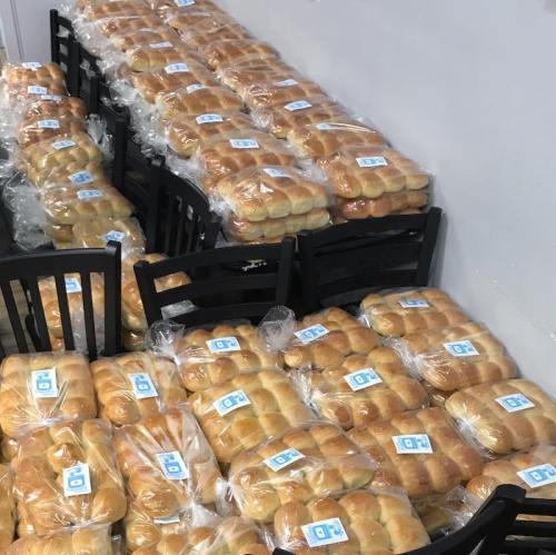 A large display of neatly packaged bread rolls stacked on tables and chairs in a bright room.