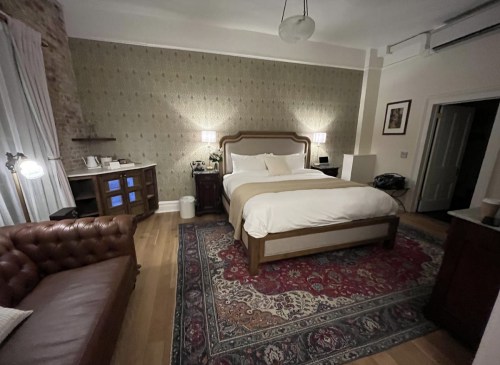 Cozy hotel room featuring a large bed, vintage decor, a leather sofa, and warm lighting.