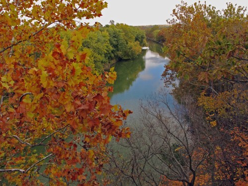A serene river surrounded by trees with vibrant autumn foliage reflecting in the water.