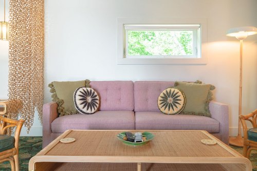 A cozy living room featuring a pink sofa with decorative pillows, a wooden coffee table, and natural light from a window.