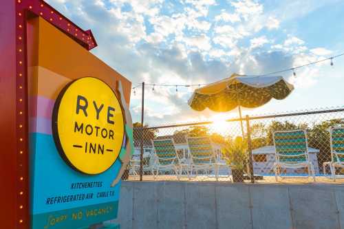 Sign for Rye Motor Inn with a pool area in the background, featuring lounge chairs and a sunset sky.