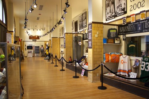 A hallway in a sports museum featuring displays of jerseys, memorabilia, and photographs along the walls.
