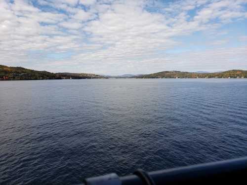 A serene view of a calm lake surrounded by hills under a partly cloudy sky.