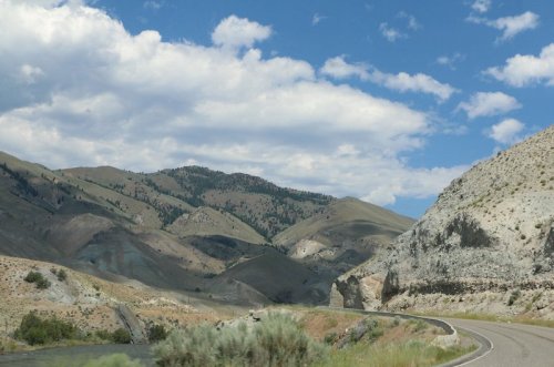 A winding road through rugged mountains under a partly cloudy sky, showcasing diverse terrain and greenery.