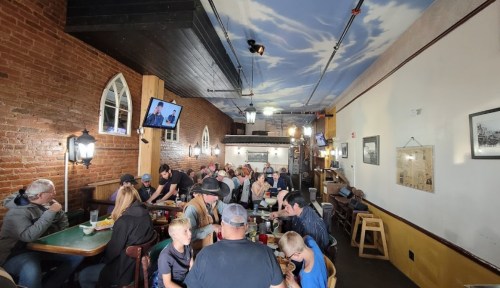 A busy restaurant interior with patrons dining at tables, brick walls, and a painted sky ceiling.