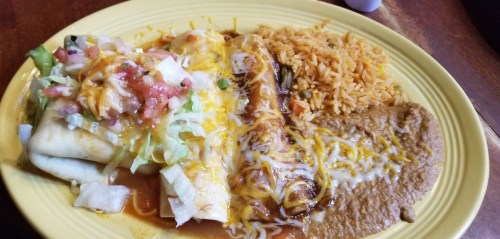 A plate of Mexican food featuring a burrito, enchilada, rice, and refried beans, topped with cheese and salsa.
