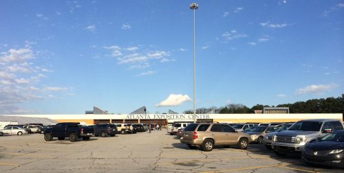 A wide view of the Atlanta Exhibition Center with a parking lot filled with cars under a clear blue sky.