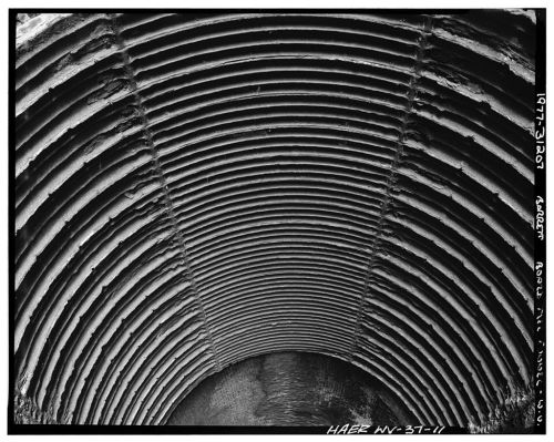 Black and white image of a circular, ribbed tunnel ceiling, showcasing a textured, industrial design.