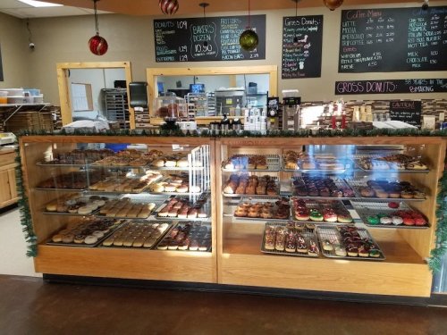 A display case filled with various donuts, decorated for the holidays, with a menu board in the background.