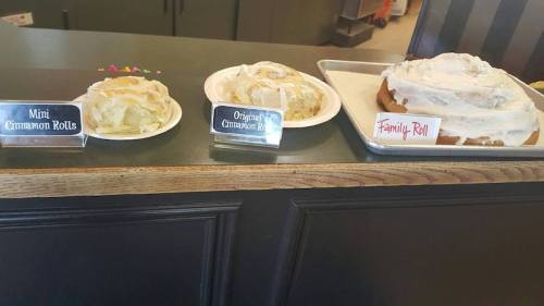 Three plates of cinnamon rolls: mini rolls, original rolls, and a large family roll, all topped with white icing.