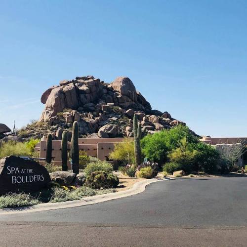 A desert landscape featuring large boulders, cacti, and a sign for "Spa at The Boulders" along a winding road.