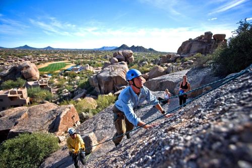 A group of climbers ascends a rocky terrain with a scenic desert landscape in the background.