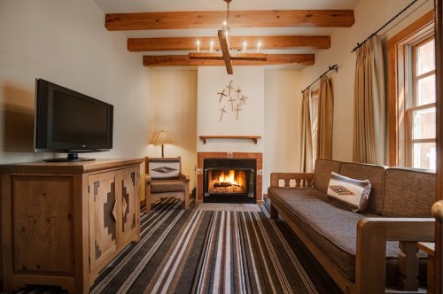 Cozy living room with wooden beams, a fireplace, TV, and rustic furniture, featuring a striped rug and warm lighting.