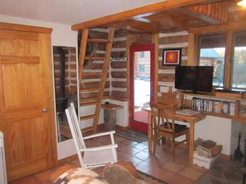 Cozy log cabin interior featuring a wooden staircase, desk, TV, and a rocking chair by the door.