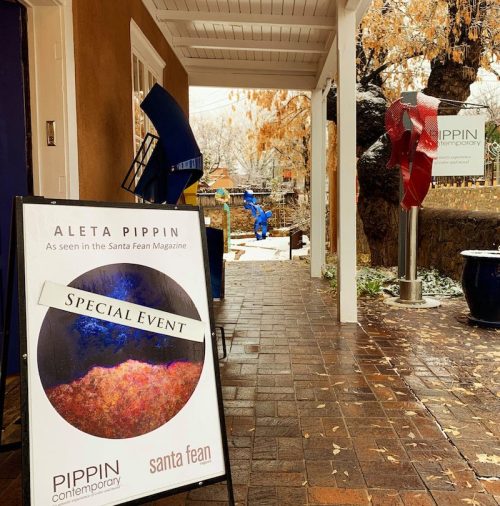 A sidewalk sign for a special event at Pippin Contemporary, featuring colorful sculptures and a rainy atmosphere.