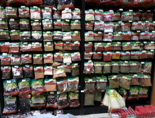 A wall of various spices and herbs in clear bags, neatly organized on shelves in a store.