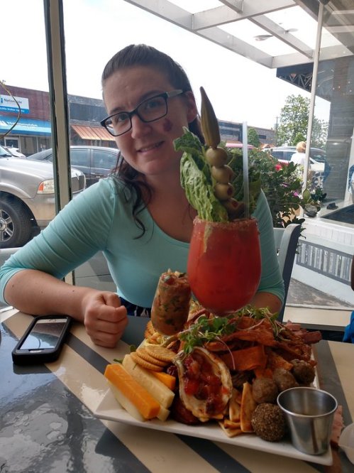 A woman sits at a table with a large, colorful platter of food, including a tall drink garnished with vegetables.