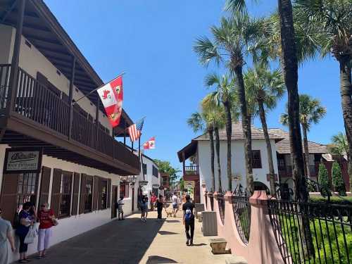 A sunny street scene with palm trees, flags, and people walking in a historic area with colonial-style buildings.