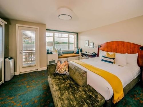 Cozy hotel room featuring a queen bed, seating area, and large windows with natural light.