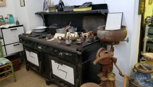 A vintage kitchen setup featuring an old stove, cookware, and various kitchen tools on display.