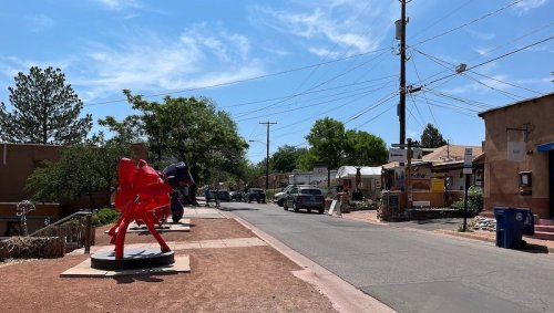 A street scene featuring red sculptures, trees, and buildings under a blue sky with power lines overhead.