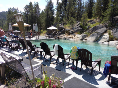 A serene poolside scene with lounge chairs, umbrellas, and rocky surroundings in a forested area.