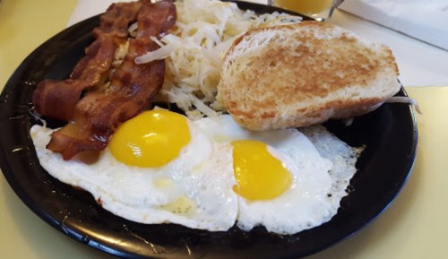 A plate with two fried eggs, crispy bacon, hash browns, and a slice of toasted bread.