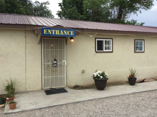 A building entrance with a sign reading "ENTRANCE," surrounded by potted plants and a gravel pathway.