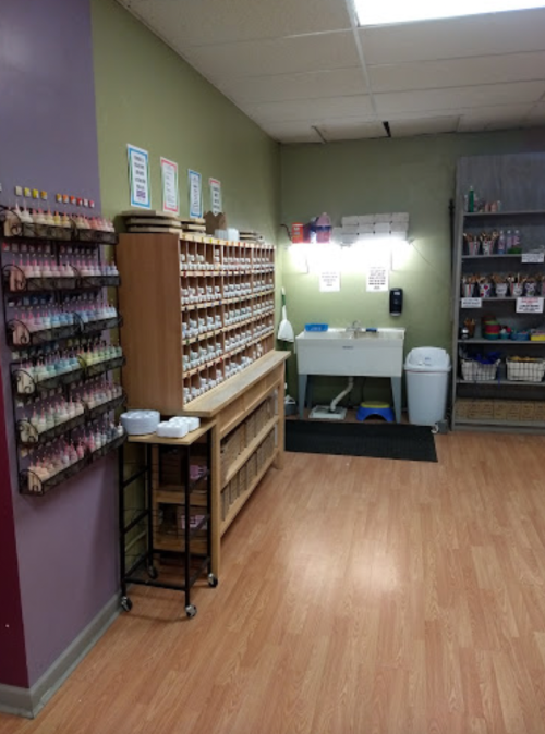 A brightly lit room with shelves of paint bottles, a work table, and storage bins on the floor.