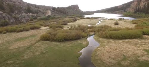 A serene landscape featuring a winding river surrounded by lush greenery and rocky hills under a cloudy sky.