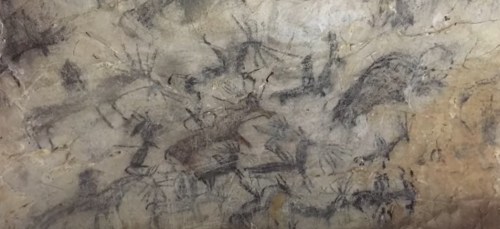 Cave wall featuring ancient petroglyphs of animals and abstract shapes, showcasing prehistoric art.
