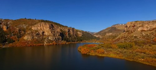 A serene landscape featuring a river winding through rocky hills and autumn foliage under a clear blue sky.