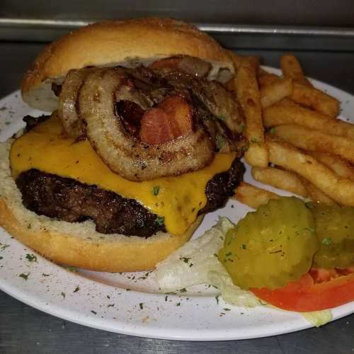 A cheeseburger topped with crispy onions, served with fries, pickles, and a slice of tomato on a plate.